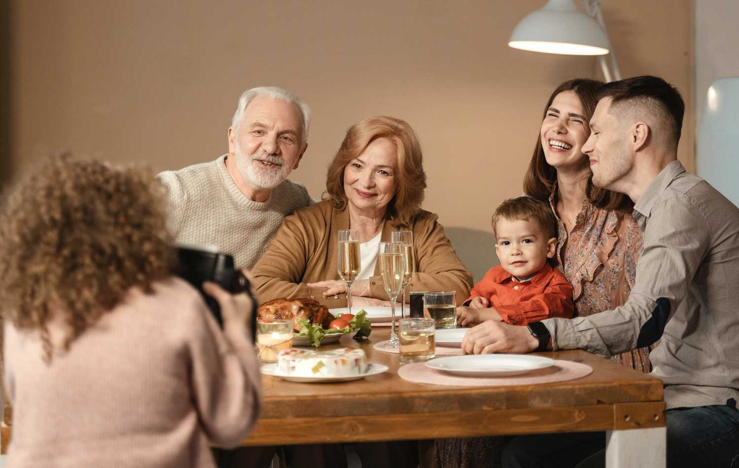 Family gathering at a holiday table, featuring smiling adults and a child, with festive food and drinks, emphasizing warmth and togetherness during the holiday season.